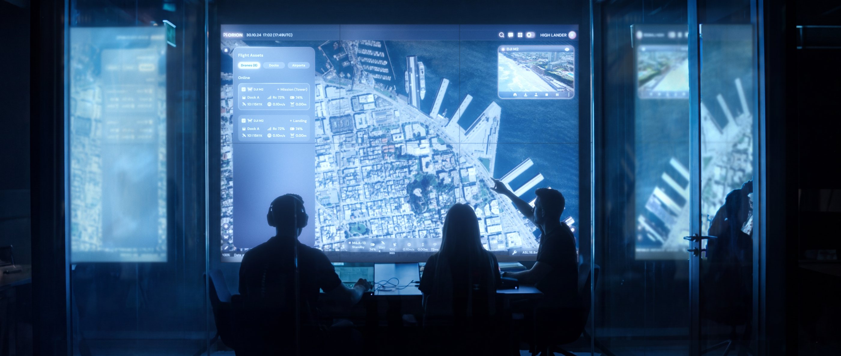 Operators in a dark control room in front of a large Orion map wall